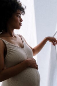 Pregnant Black mother peeking behind curtains