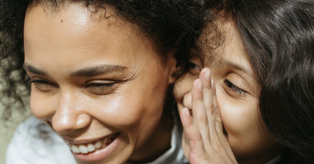 Little girl whispering a secret to a smiling woman