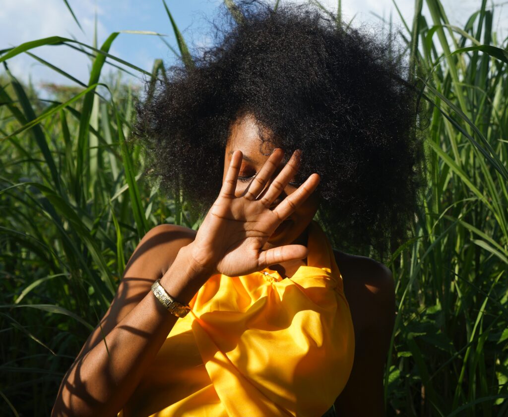 Shy Black woman with natural hair holding her hand in front of her face