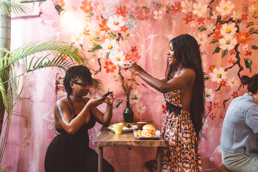 Two Black women taking pictures of their meal while out to dinner
