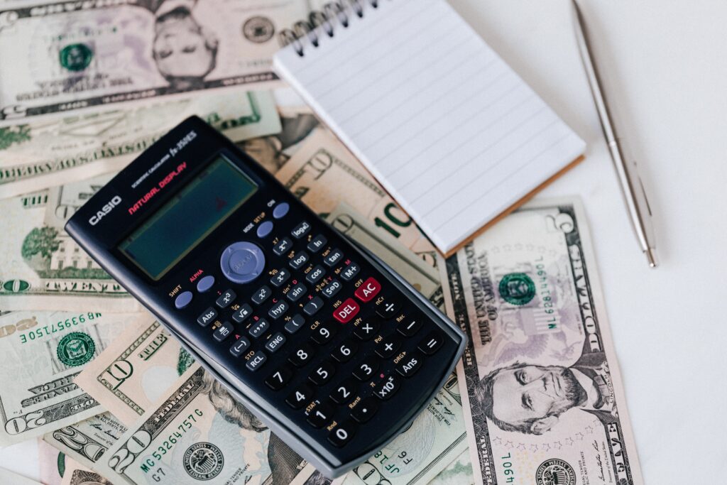 A calculator, notepad, and pen sitting on top of several dollar bills.