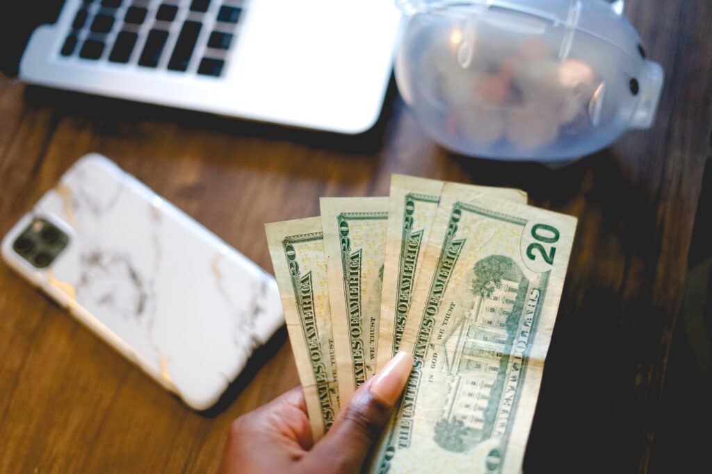A hand holding several $20 bills over a piggy bank.