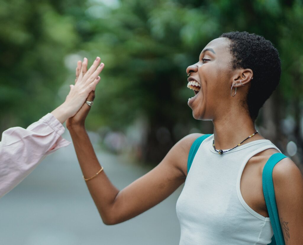 A Black woman giving someone a high-five while laughing.