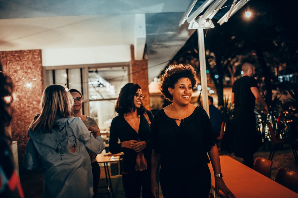 A Black woman smiling as others around her mingle at an event.
