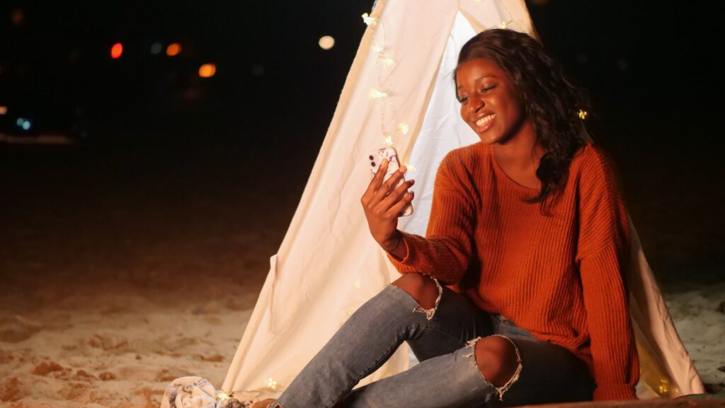 Black woman on a virtual call while in front of a tent at the beach