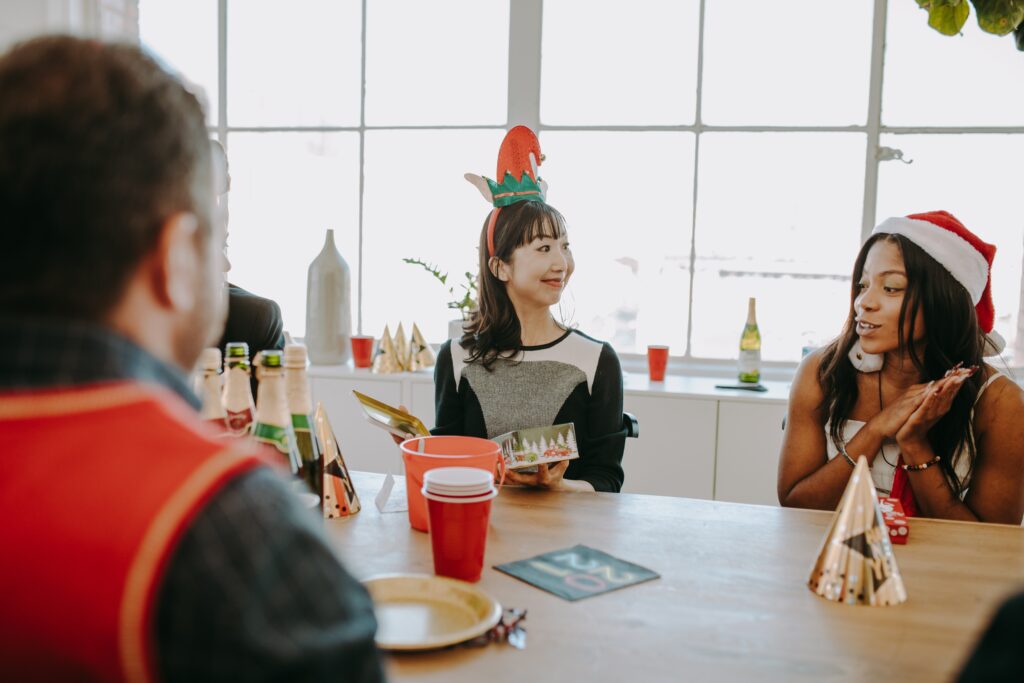 Three employees smiling at each other as they sit down for a holiday party.
