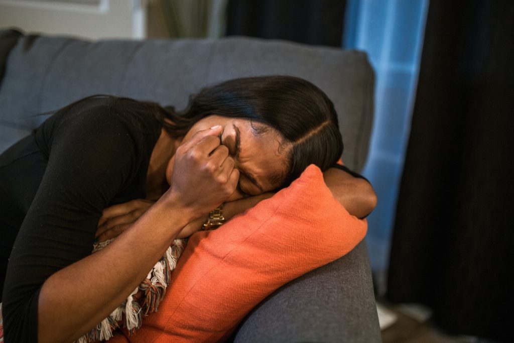 Black woman crying into a pillow on the couch