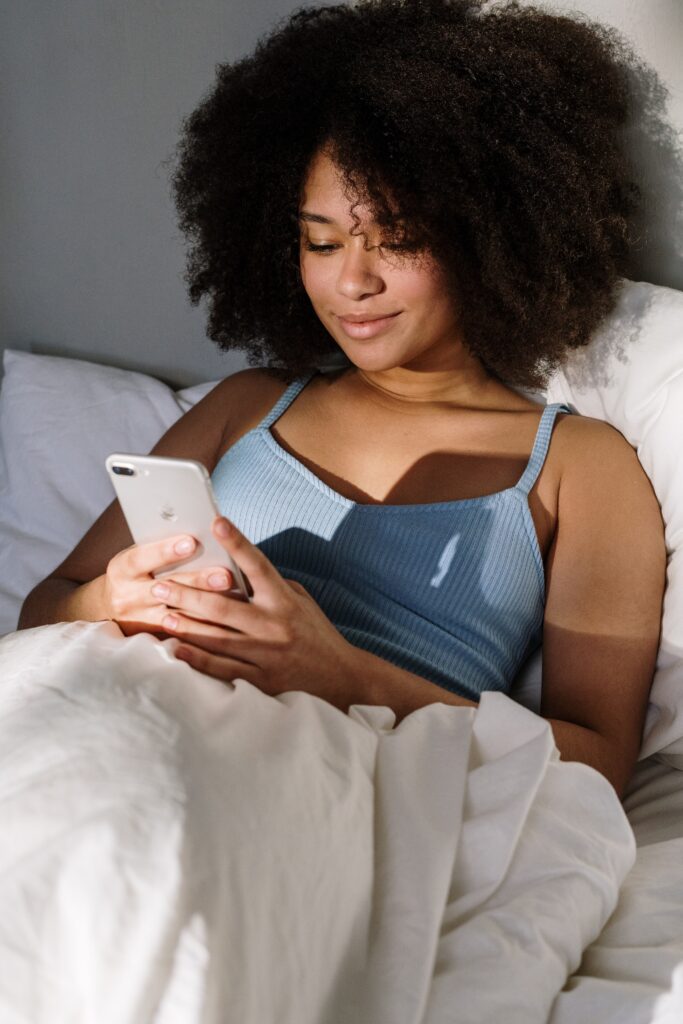 Black woman looking at her phone while on the bed