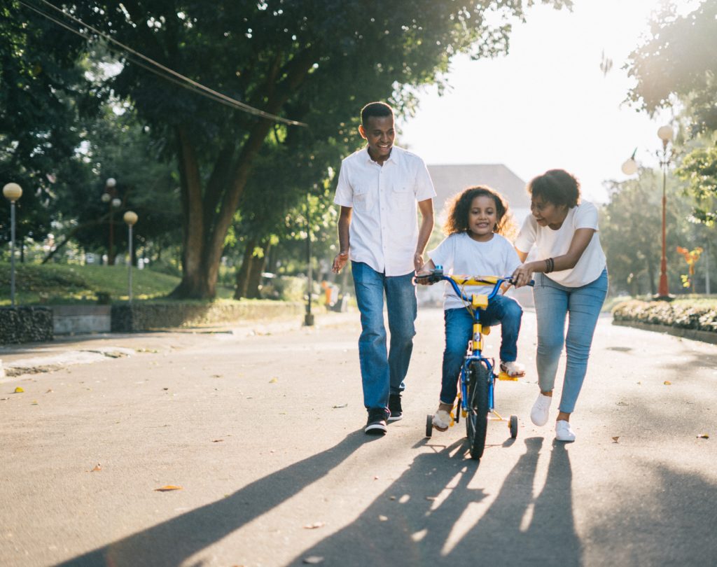 Black parents teaching their daughter how to ride a bike in the neighborhood