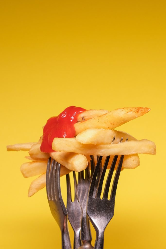 Several forks holding up french fries topped with ketchup