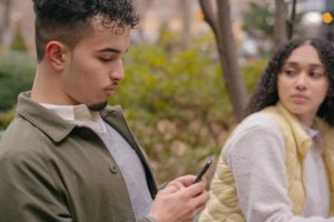 Upset woman looking at her partner who's preoccupied with his phone