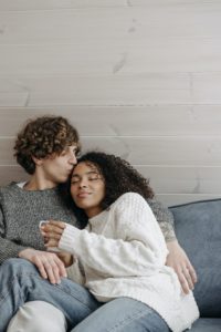 Cheating man kissing his girlfriend's forehead as they sit on the couch