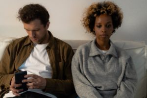 Upset Black woman sitting next to her partner who's preoccupied with his phone