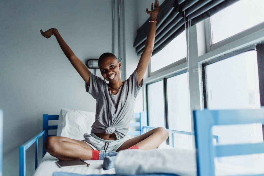 Smiling Black woman with a shaved head sitting on a bed