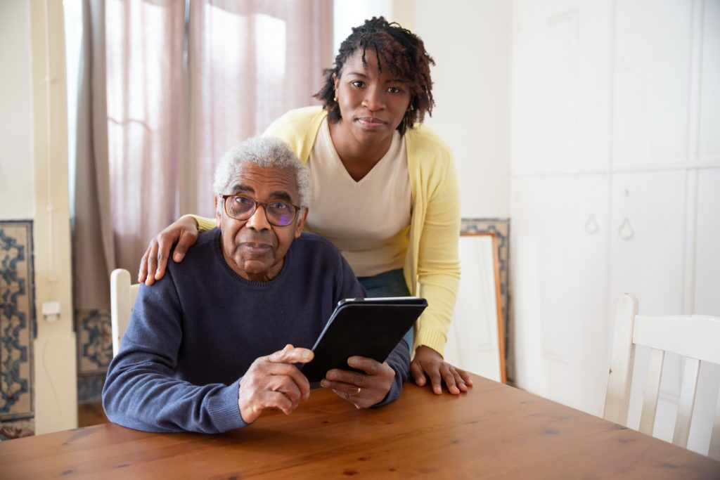 Smiling Black woman standing over an elderly Black man