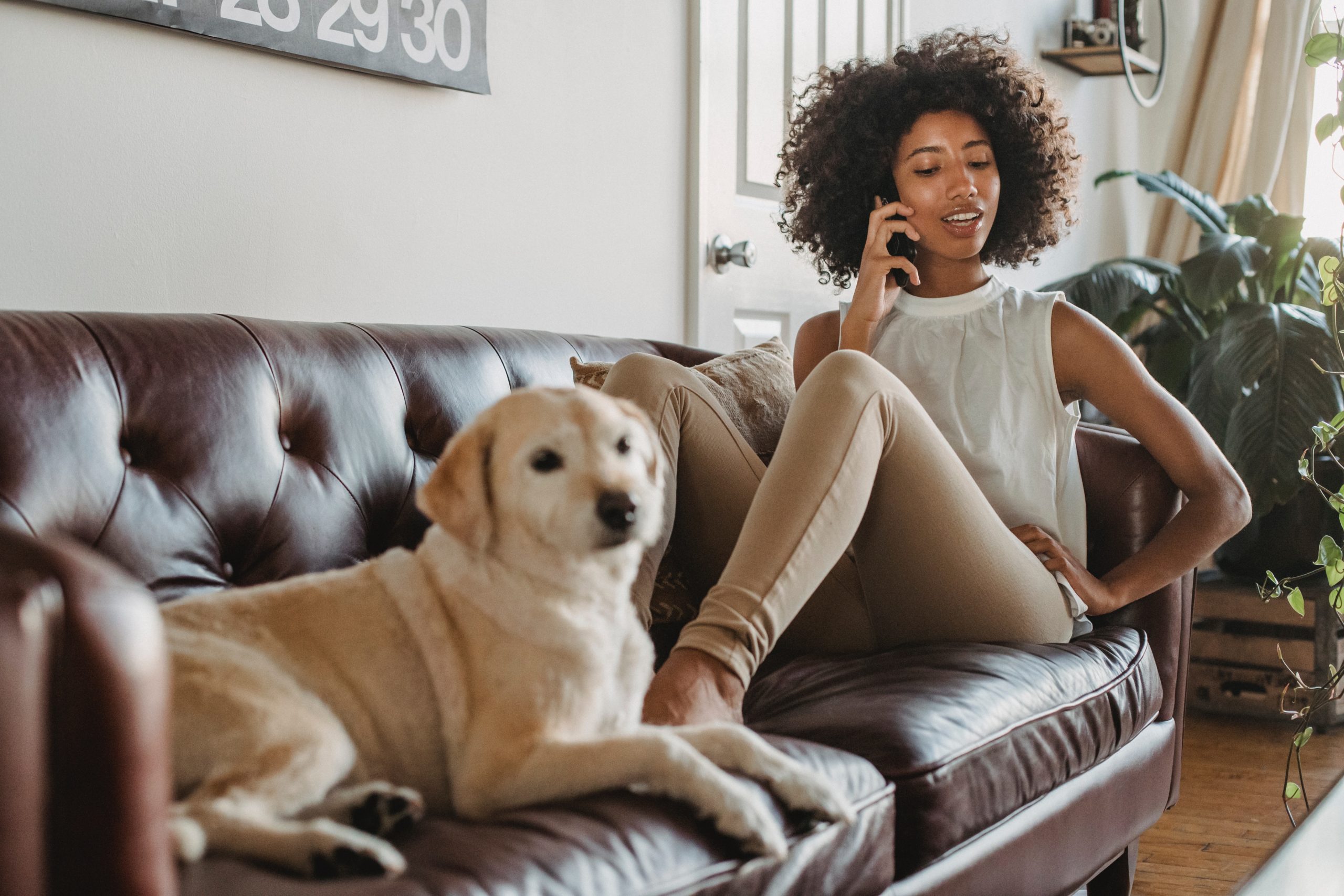 Black women talking on the phone while sitting on the couch with her dog