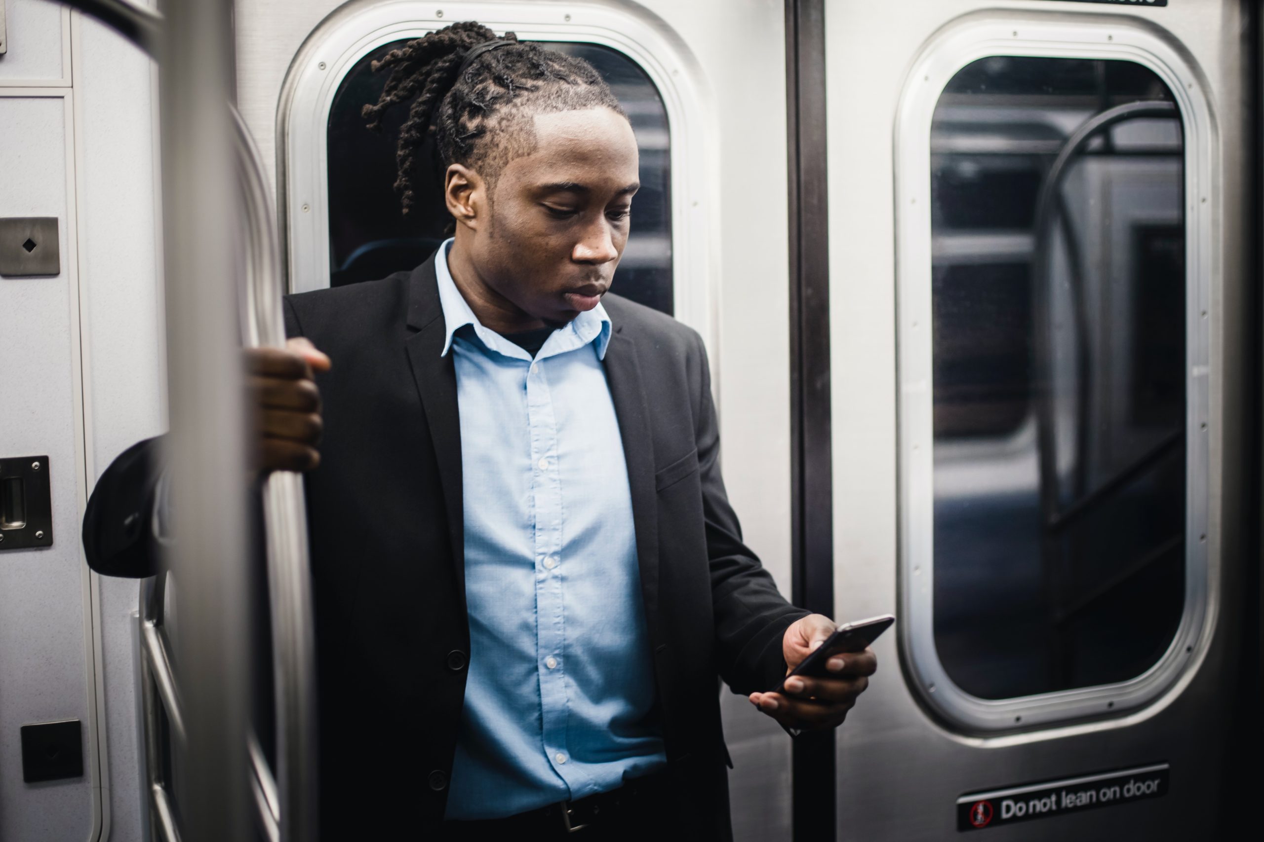 Black man staring down at his phone while on the subway