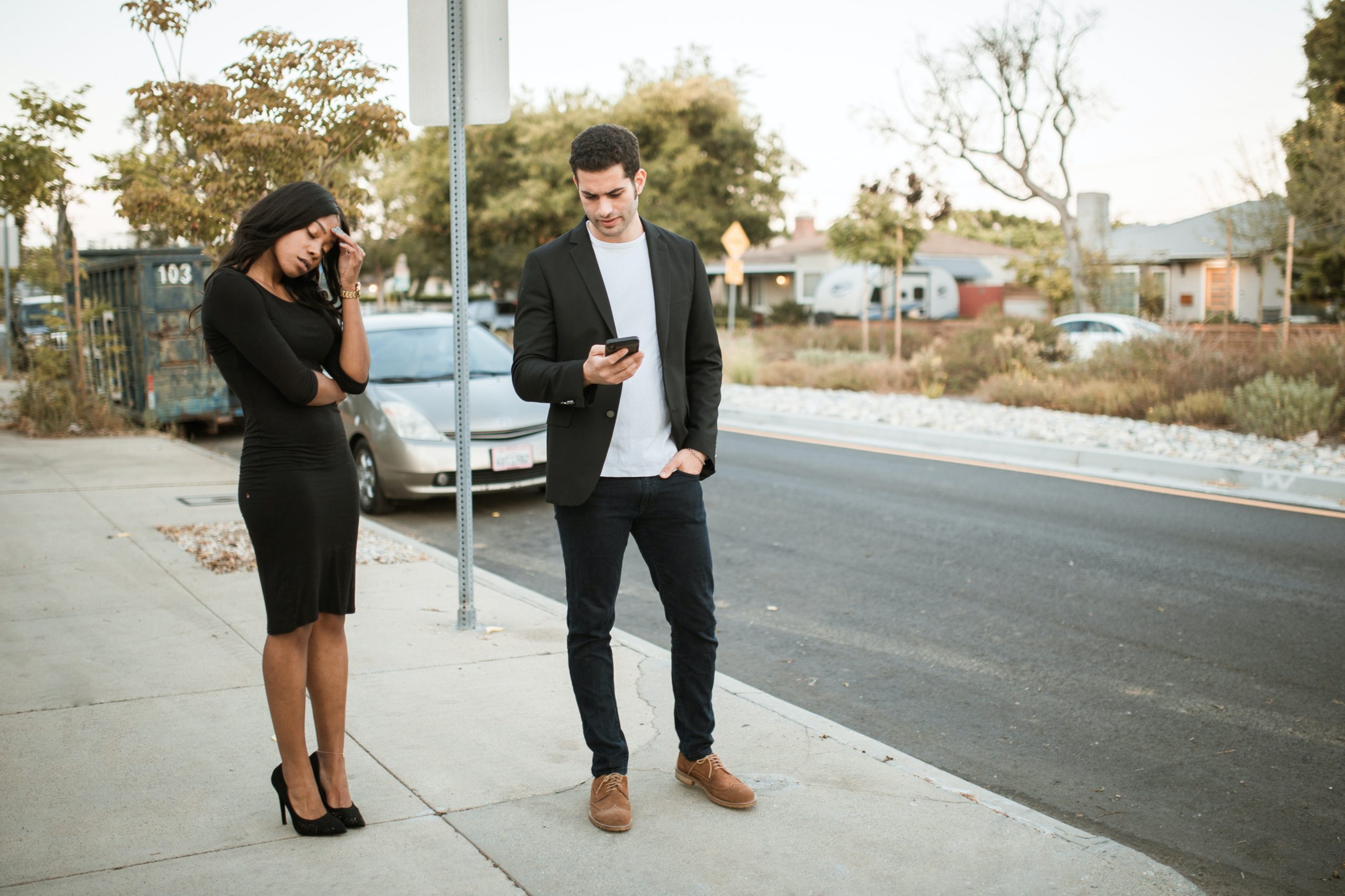 Frustrated Black woman standing next to her partner who's distracted by his phone