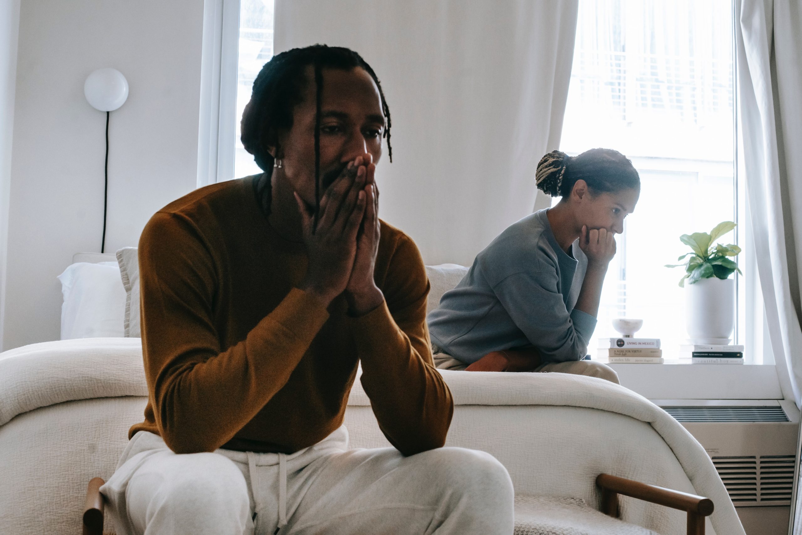 Frustrated Black couple sitting on either side of the bed