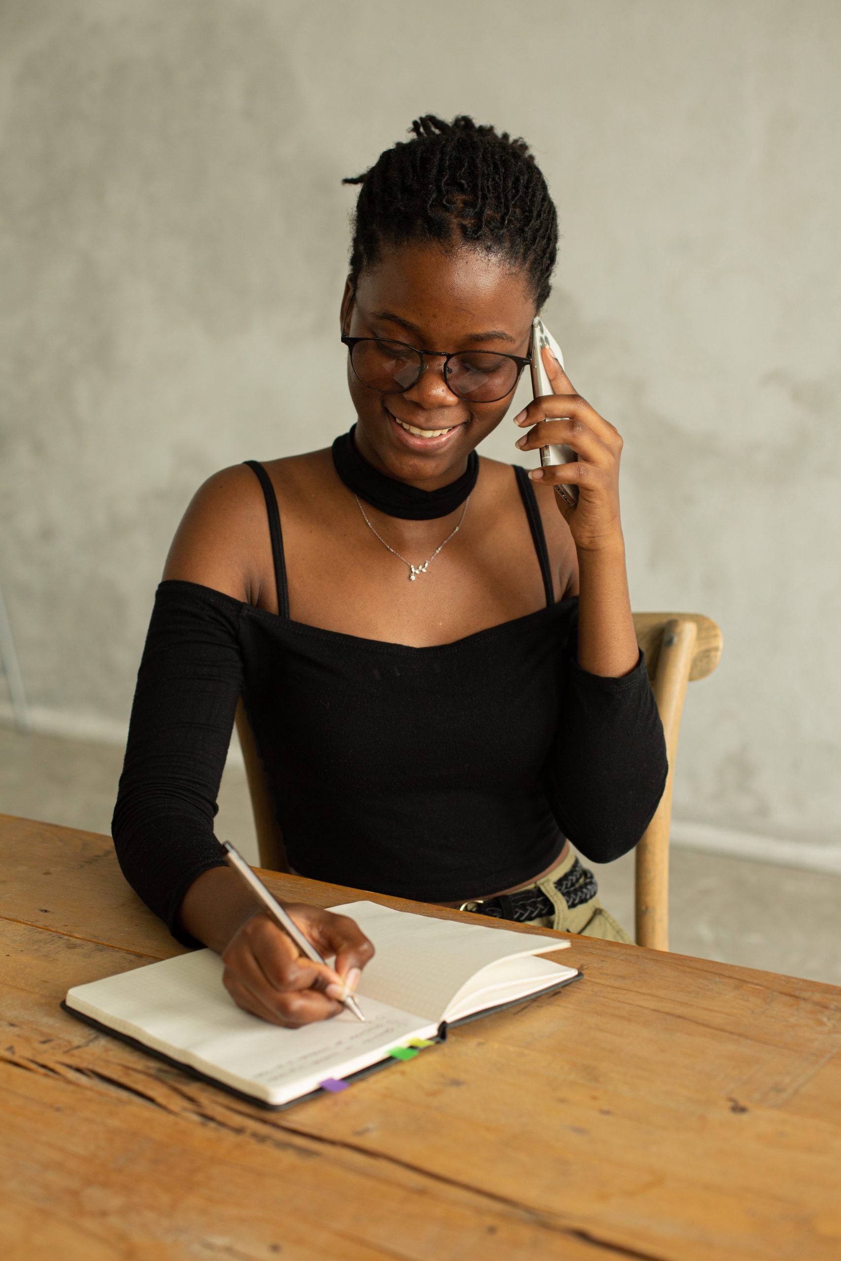 Smiling Black women jotting notes as she talks on the phone