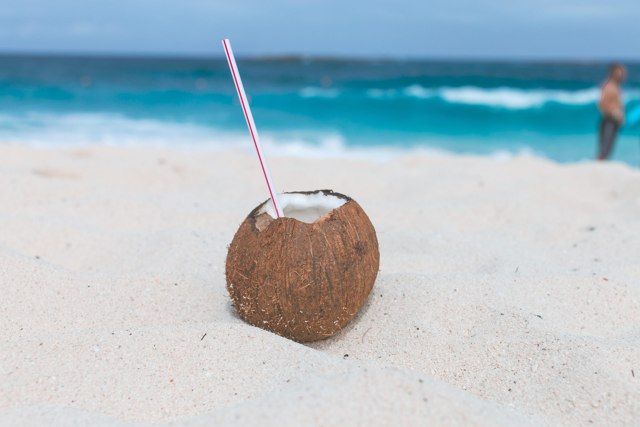 A closeup of a coconut drink nestled in the sand at the beach