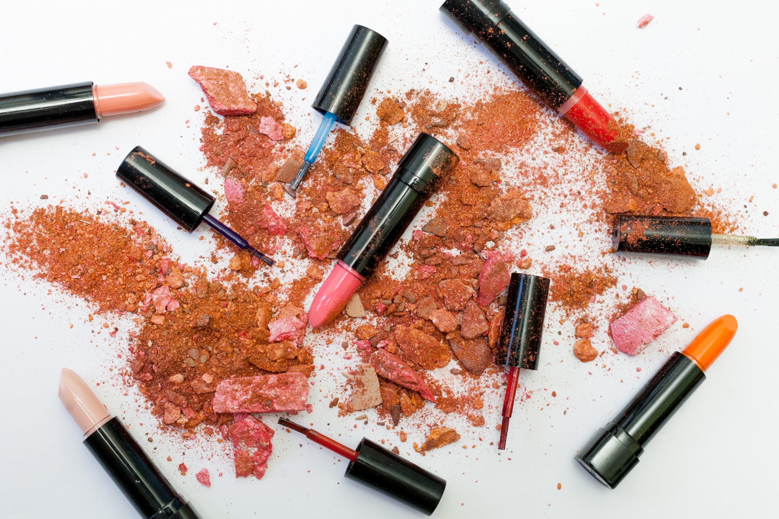 Broken makeup powders and colorful lipsticks in front of a white background