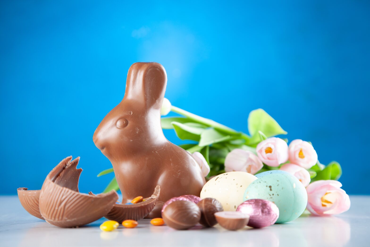 chocolate rabbit and wrapped chocolate candy with pastel flowers in back