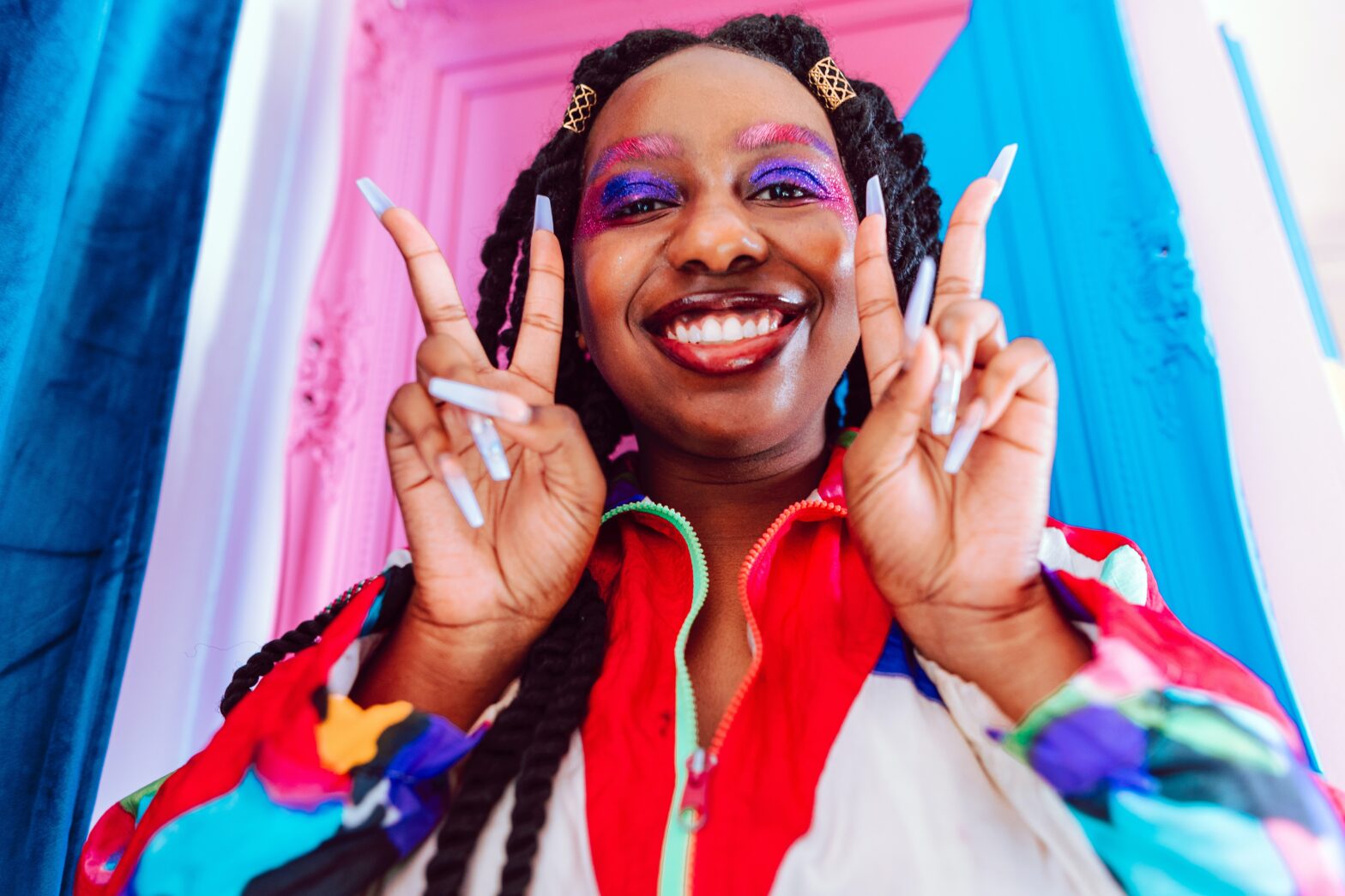 black woman in front of pink door with colorful make up and peace sign hands