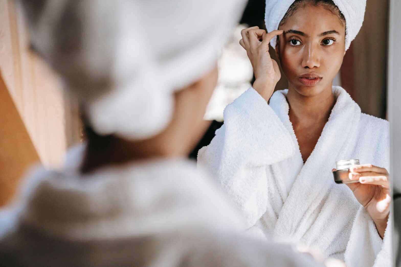 Black woman in robe putting cream on face