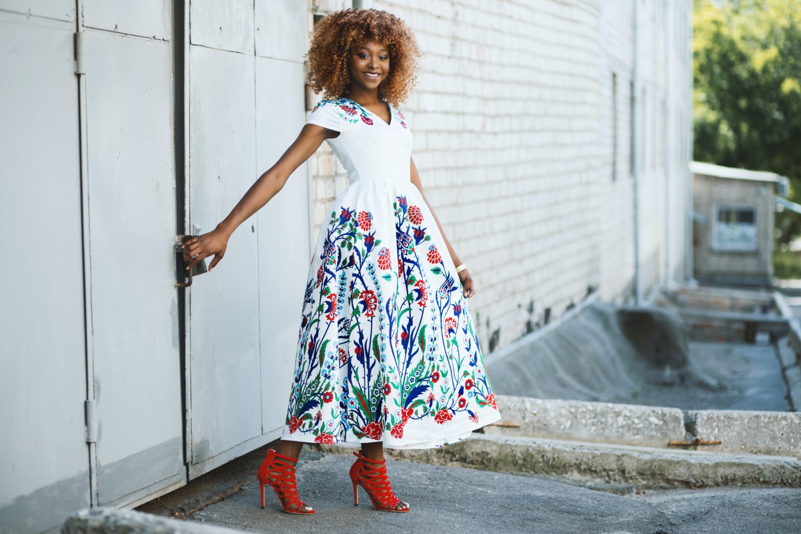 black woman in floral dress and red shoes standing outside