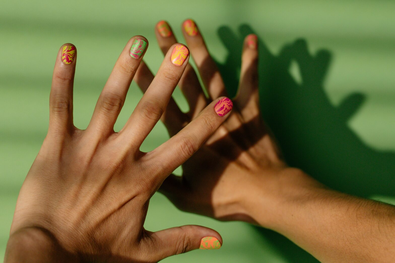 Black person hands with swirl nail polish on green background