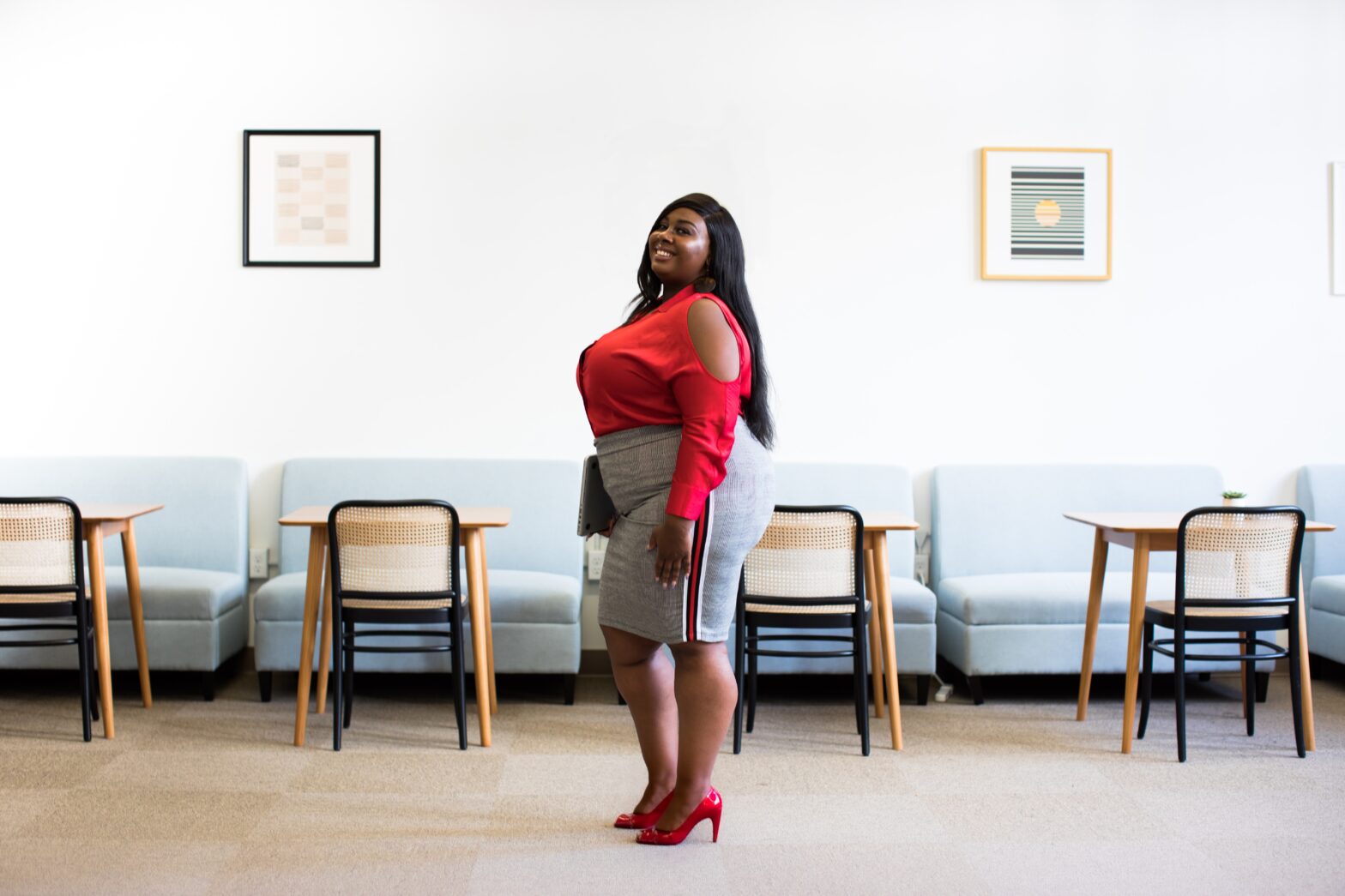 Black woman in grey pencil skirt and red top in an office lobby with chairs in the back