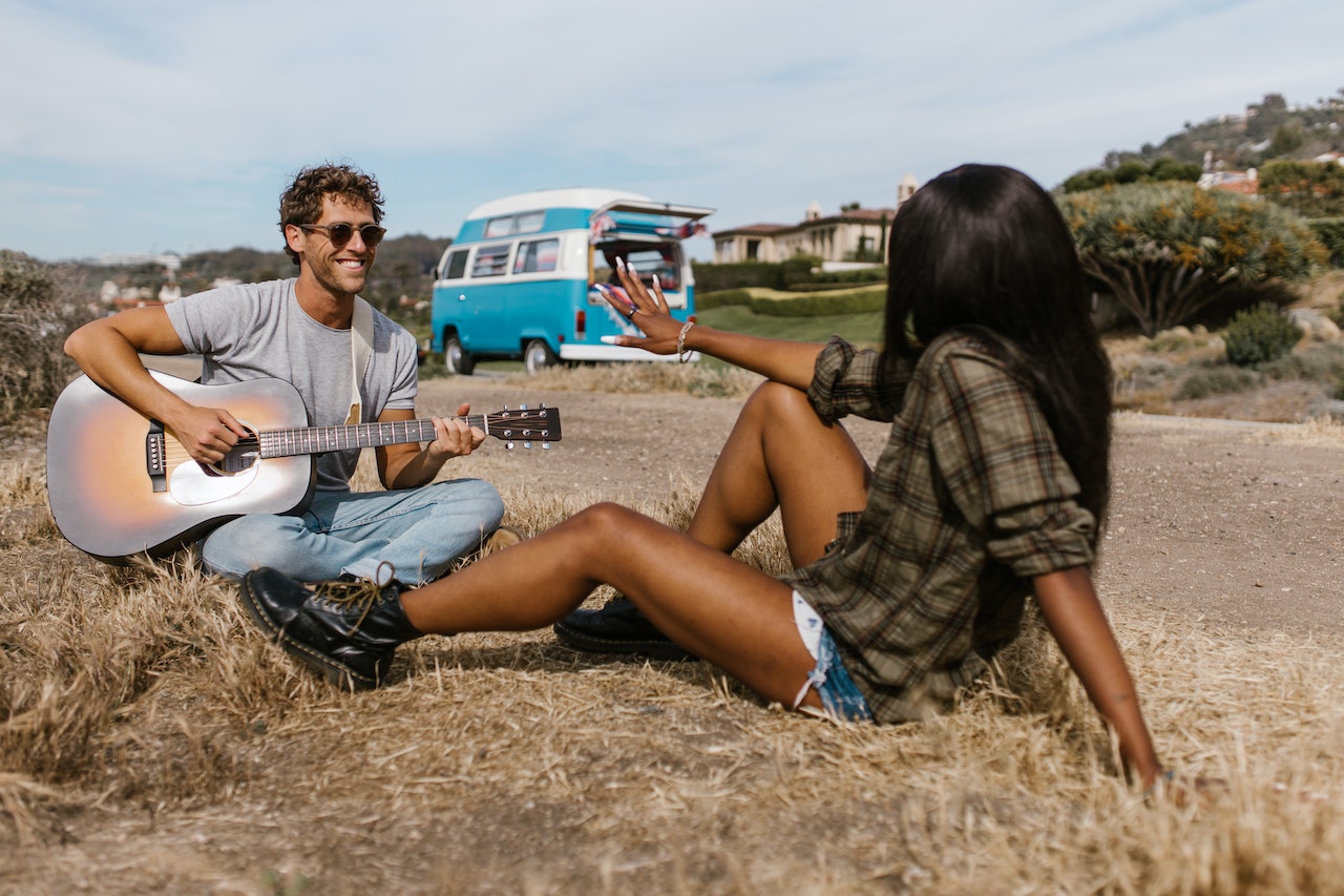 100 smooth pick up lines to use on the cute stranger you have been too afraid to approach. Pictured: A man sitting on the ground playing a guitar with a woman sticking her hand sitting across from him.