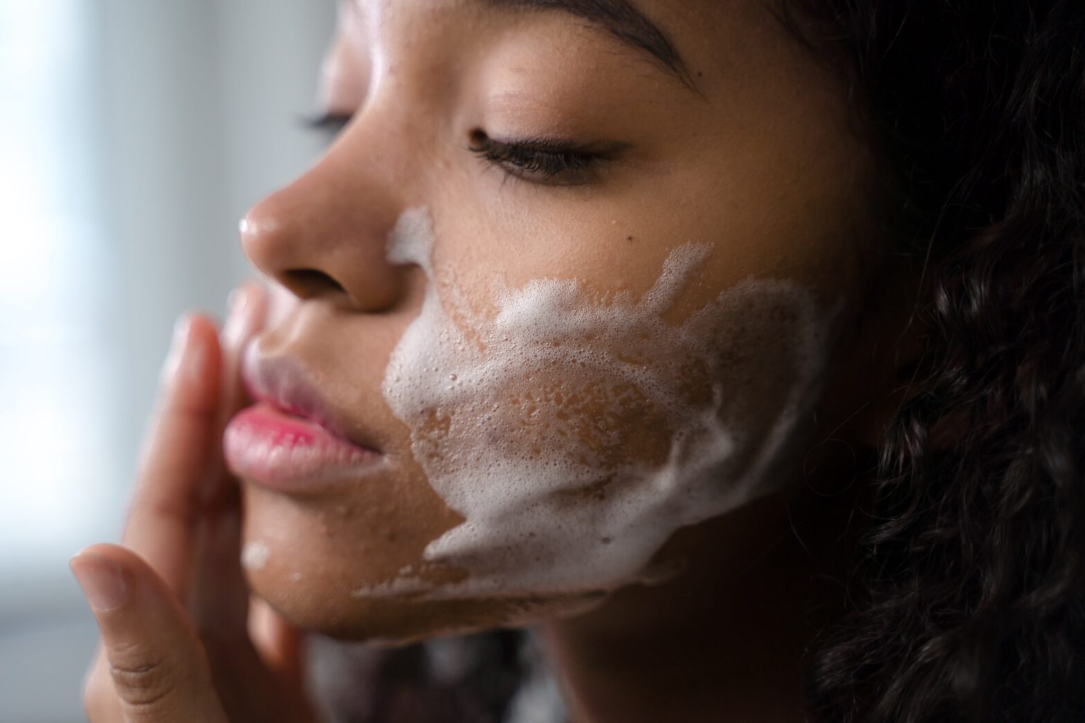 Close-up shot of a curly-haired woman cleaning her face. Retinol is proven to help skin by clearing up acne and helping with elasticity. Take a look at these retinol before and after pictures.