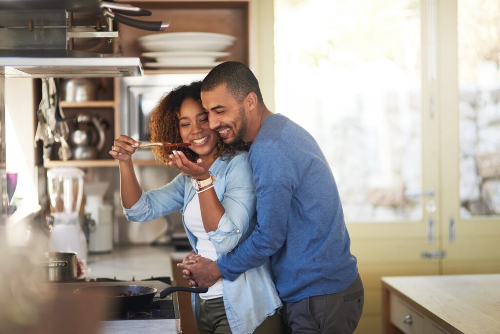 Man embraces woman from behind while standing in the kitchen