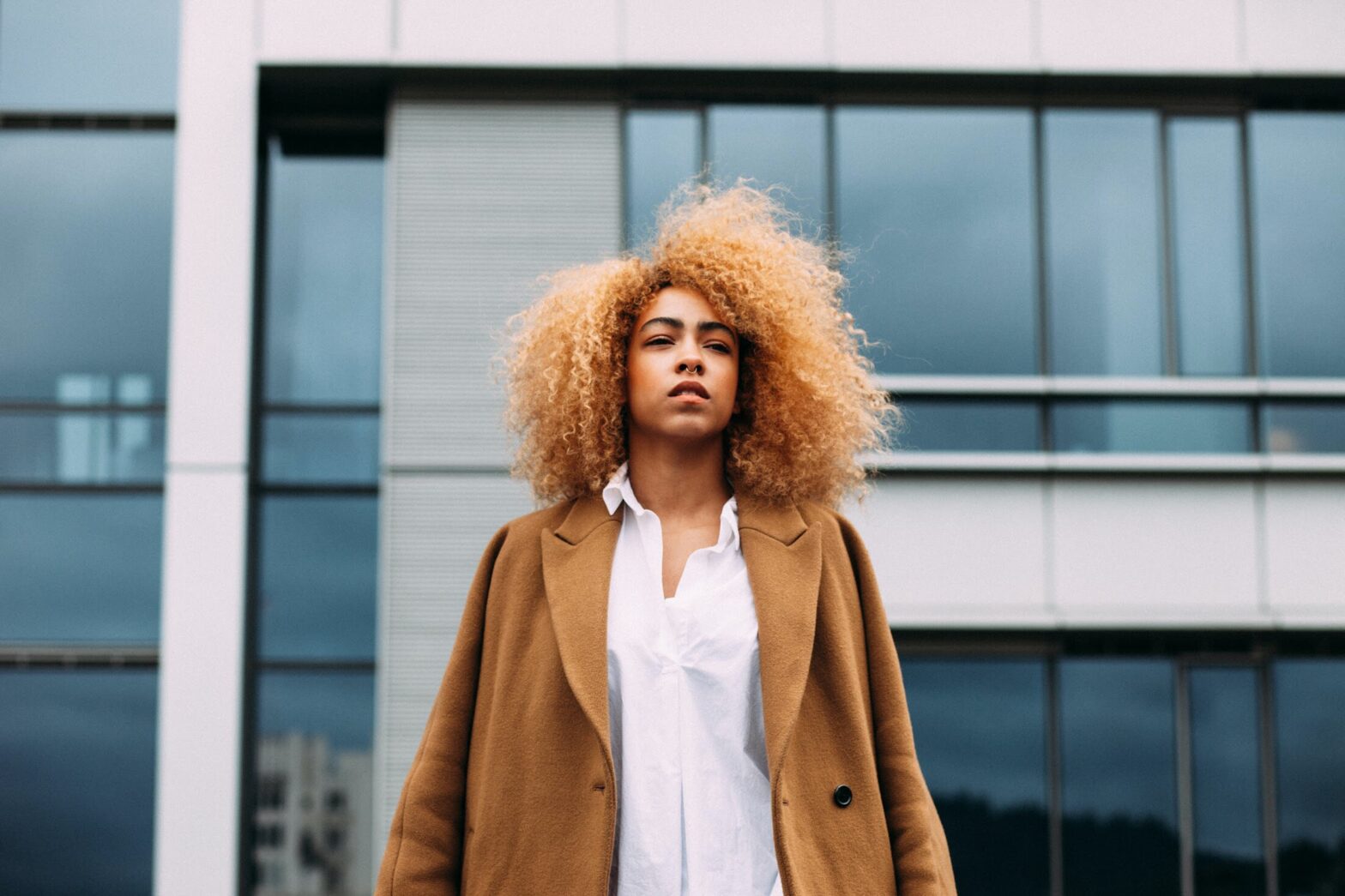 A woman with an afro standing outside in her trench coat