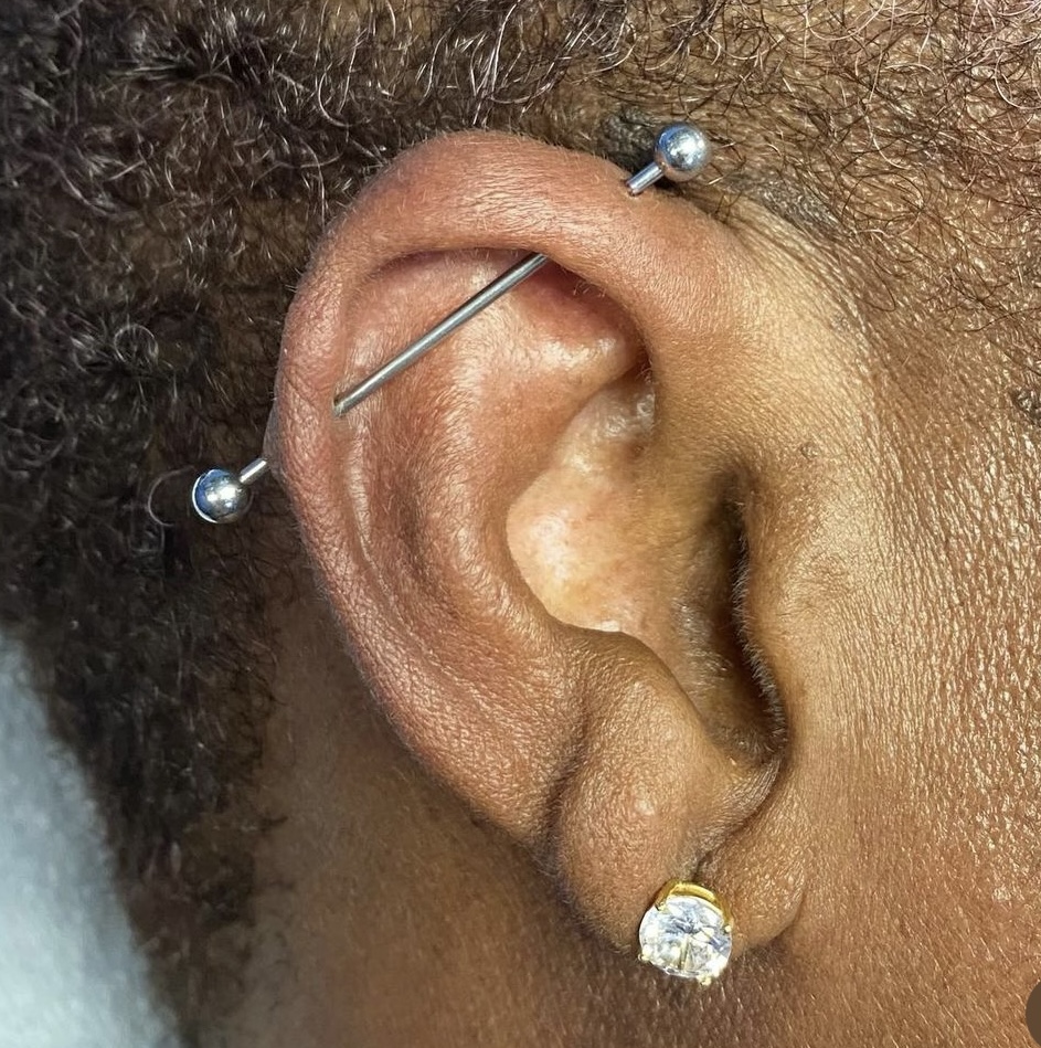 Where industrial piercings rank in most painful piercings. pictured: black girl ear with industrial piercing 