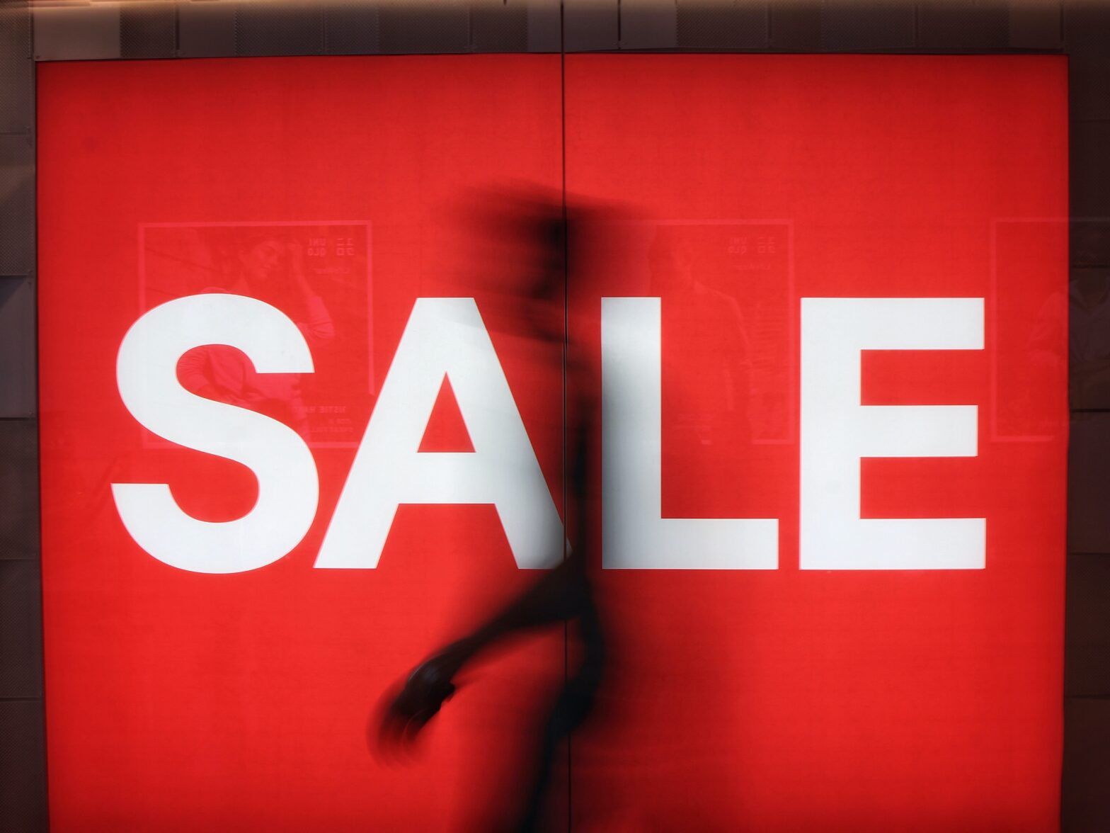 Large red sale sign with human figure moving in background