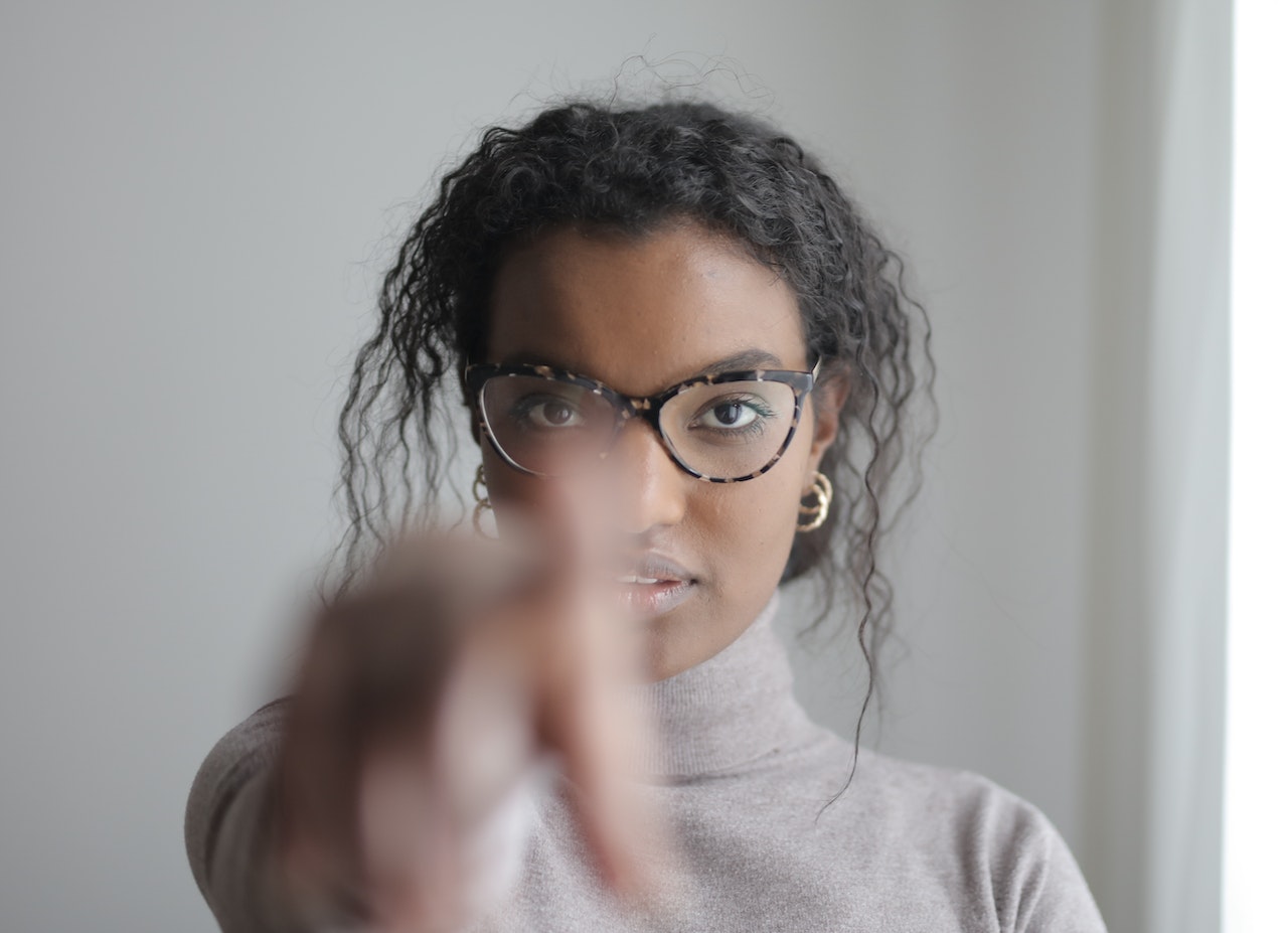 Here is a list of 100 "you got this" quotes for when you or a loved from needs that reminder. Pictured: a woman wearing glasses looking directly in the camera and pointing forward.