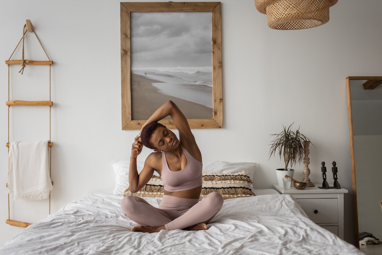 A woman stretching on top of her bed. One of the best ways to combat PCOS belly is by regularly exercising and being mindful of stress levels.