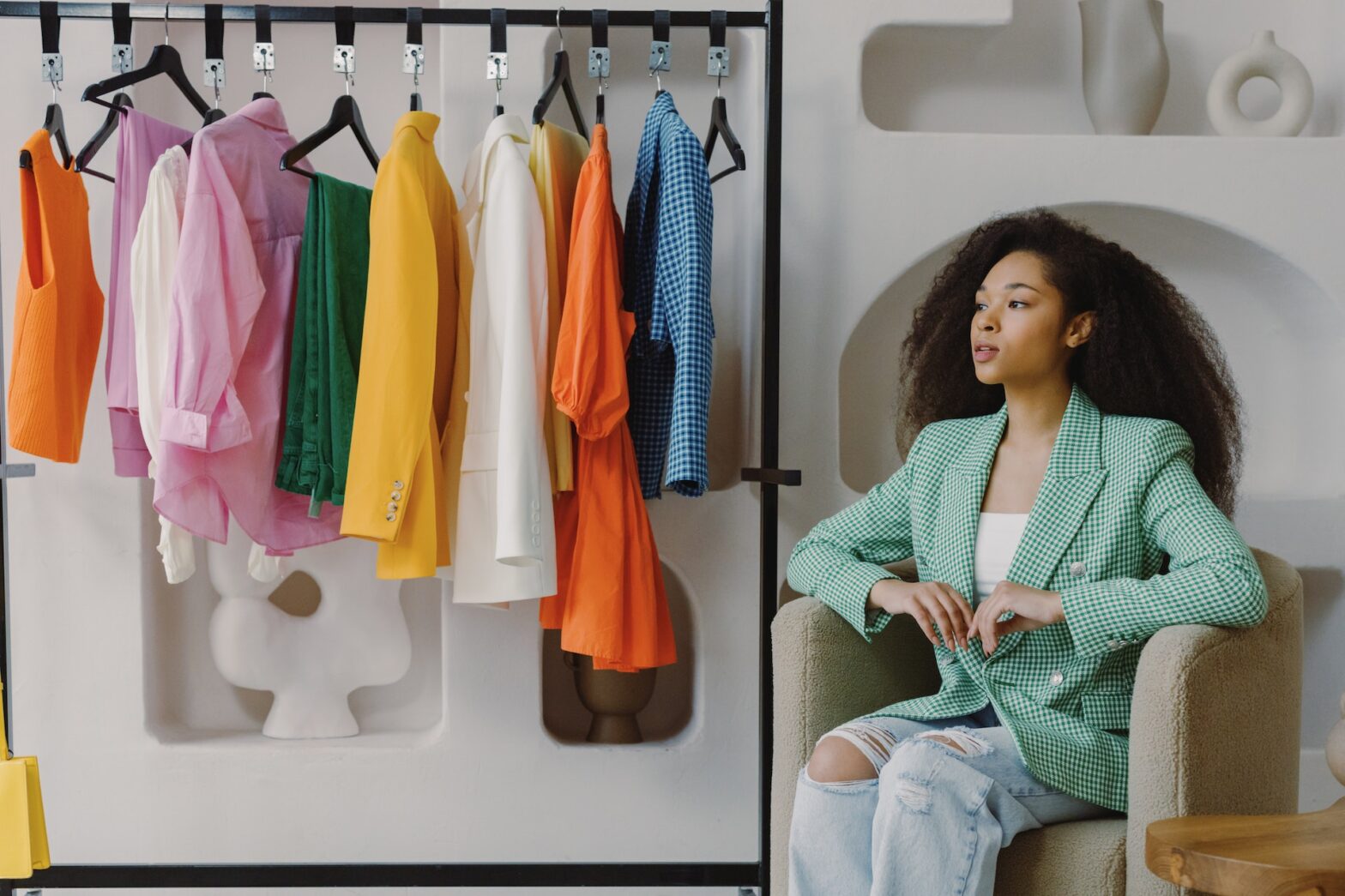 A woman in a blazer sitting next to a rack of clothes