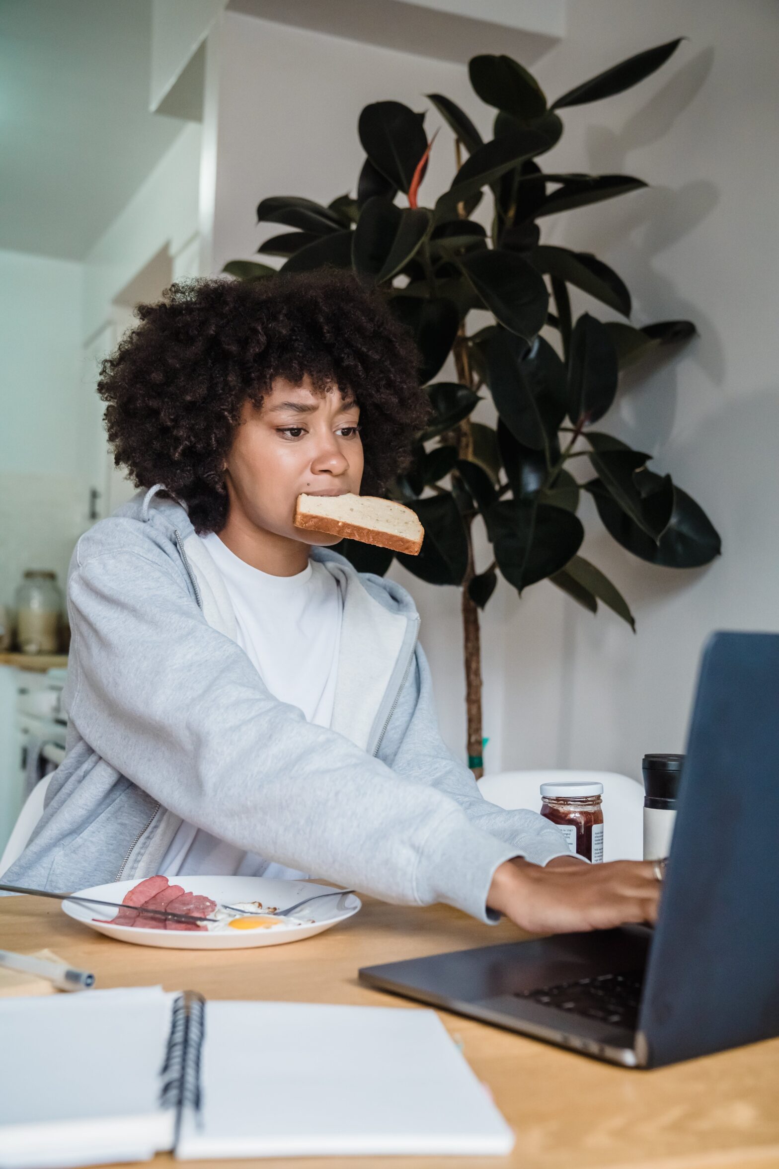 A woman eating a slice of bread as she works from her desk