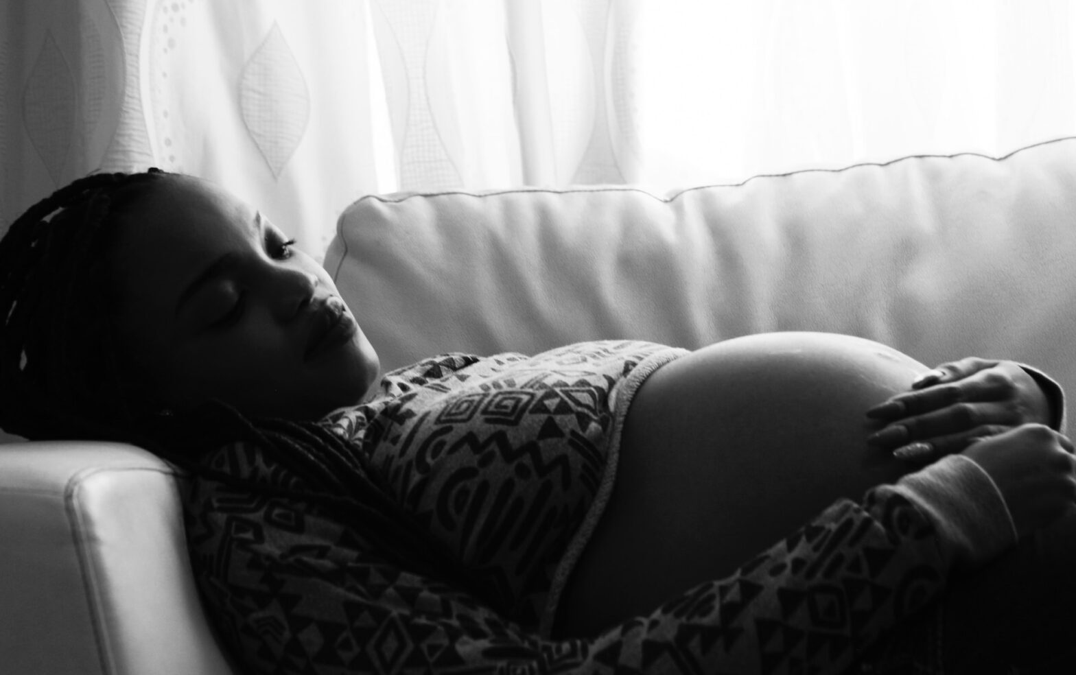 Here is your guide on How To Use A Pregnancy Pillow. Pictured: a black and white picture of a pregnant woman on a couch.