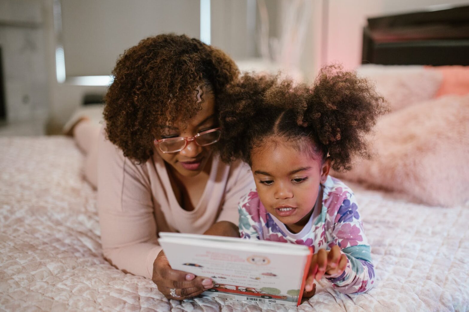 A mom and her daughter reading a book together in bed