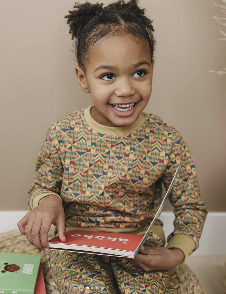 A little girl smiling as she looks up from a book