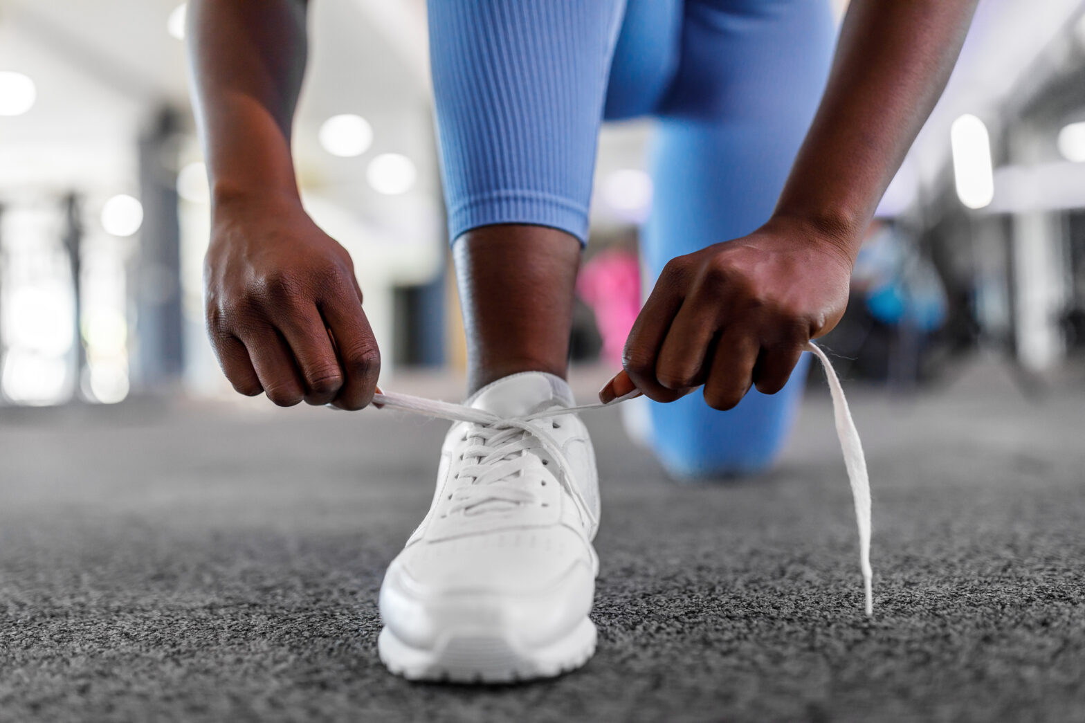 A young female athlete is tying shoelaces in a gym.
