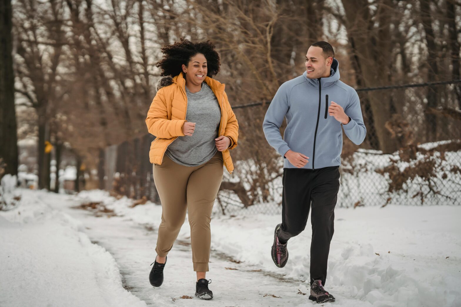 joyful-multiethnic-trainer-and-woman-running-in-winter-park