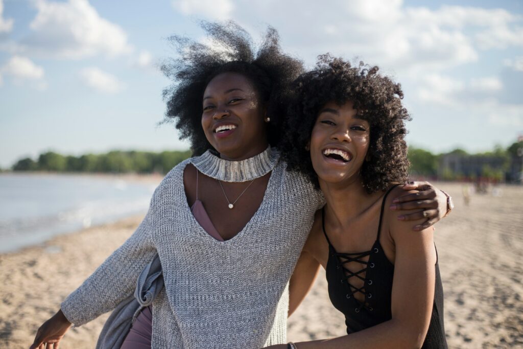 Plan a weekend getaway to the beach or mountains with your friends for this Galentine's Day idea. Pictured: Two Black women enjoying the beach