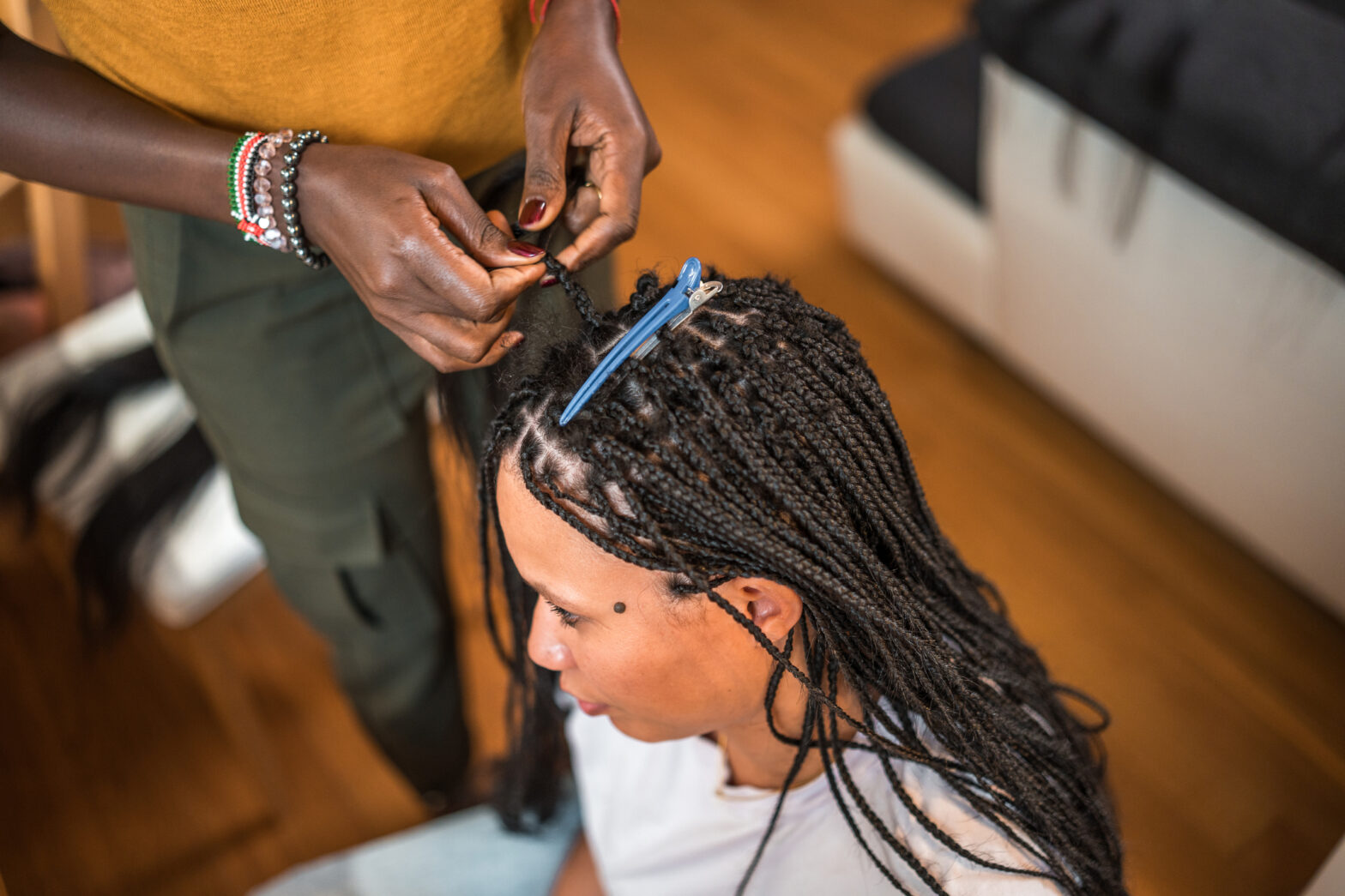 A professional mid-adult Black female hairstylist diligently works on braiding the hair of a Mixed race female client in a home setting.