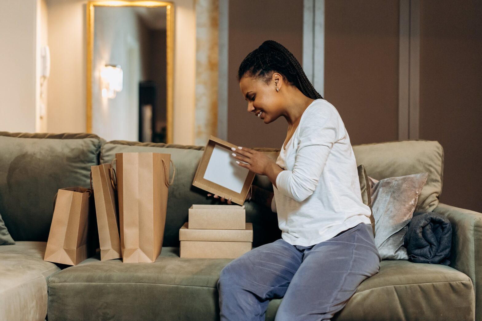 Black-woman-sitting-on-couch-opening-brown-boxes-and-paper-bags